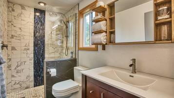 Un baño moderno con ducha de vidrio, inodoro blanco, un lavabo grande y repisas de madera sobre el espejo.