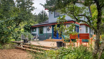A house with a wooden deck, a blue door, and a garden area with chairs and a table.