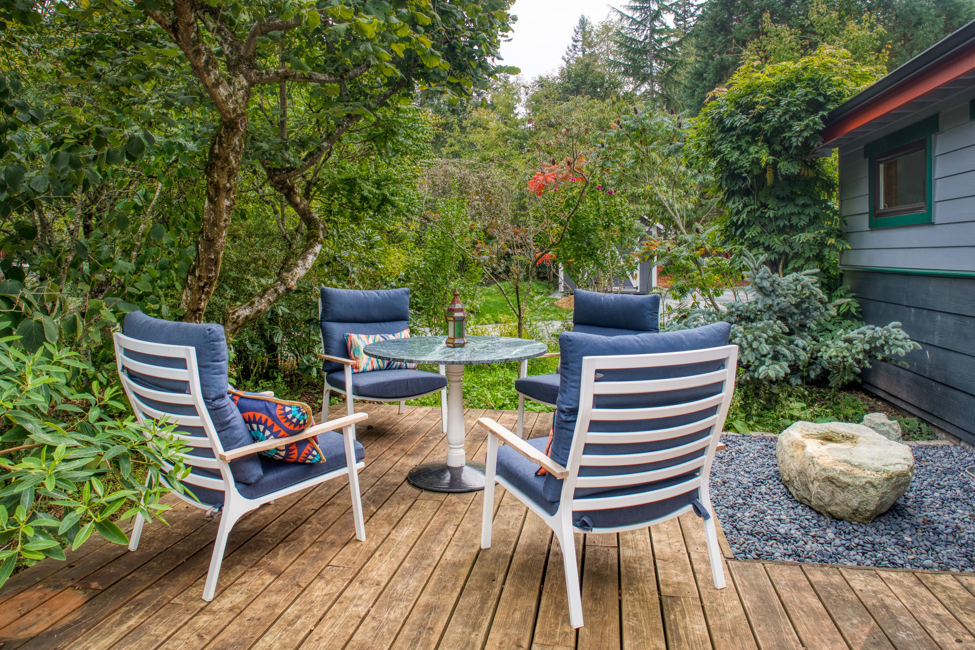 Eine Holzterrasse mit Gartenmöbeln, umgeben von üppiger Bepflanzung und einem kleinen Garten.