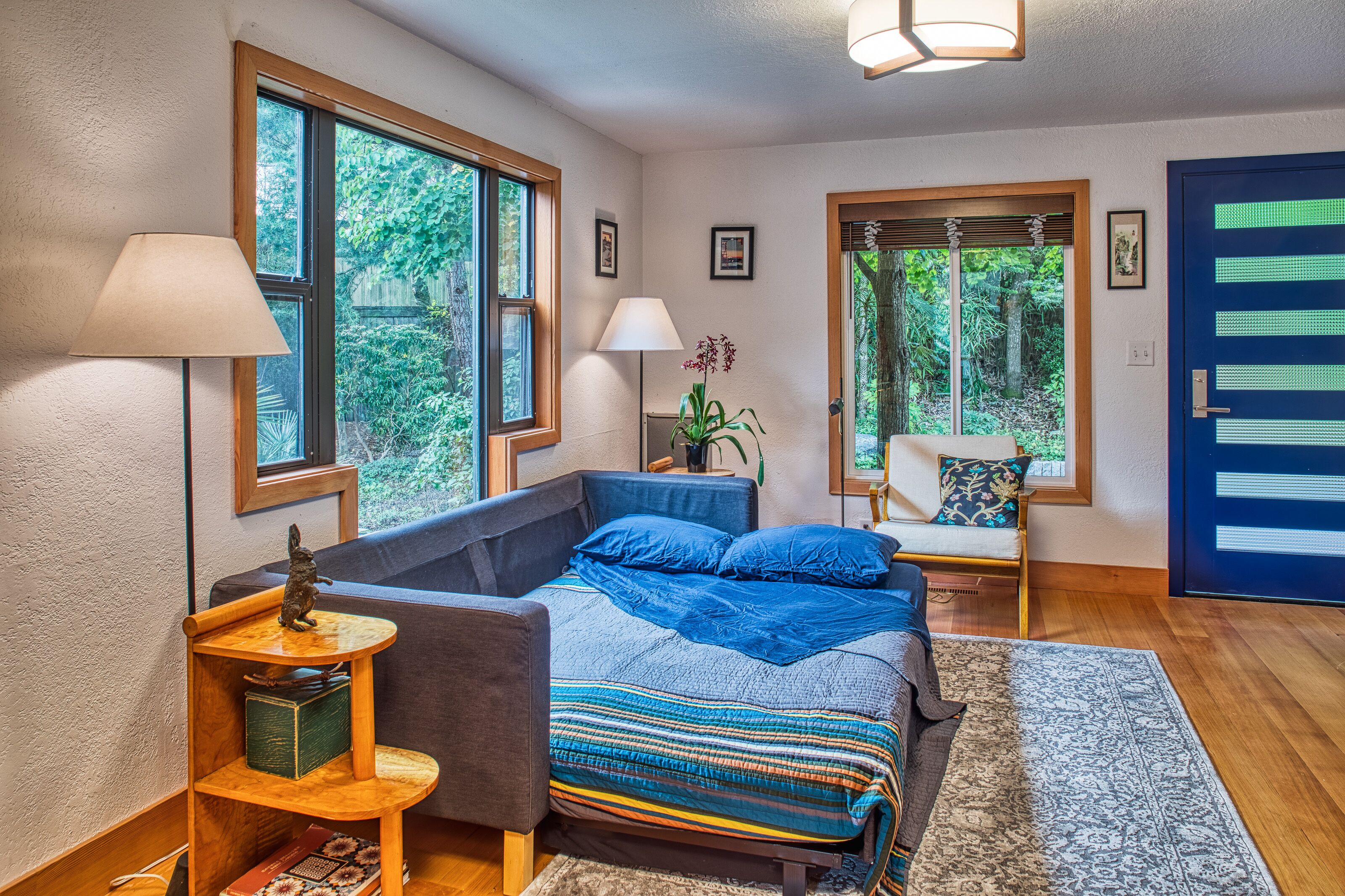 A bedroom with a bed, a chair, a lamp, a small table, and a door.