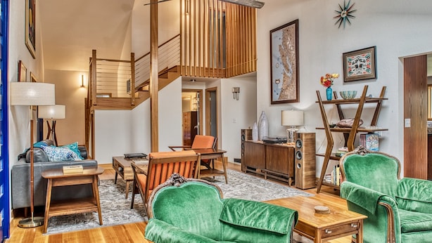 A spacious living area with a wooden staircase, a dining table, green upholstered chairs, and a bookshelf. - Sehome Garden Inn (Bellingham)