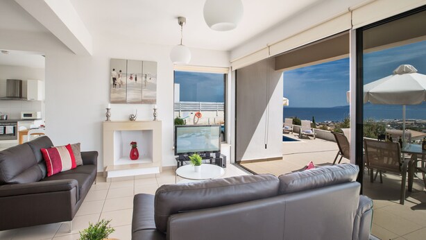 Un salon moderne avec un canapé, un téléviseur et un coin repas offrant une vue sur la mer.