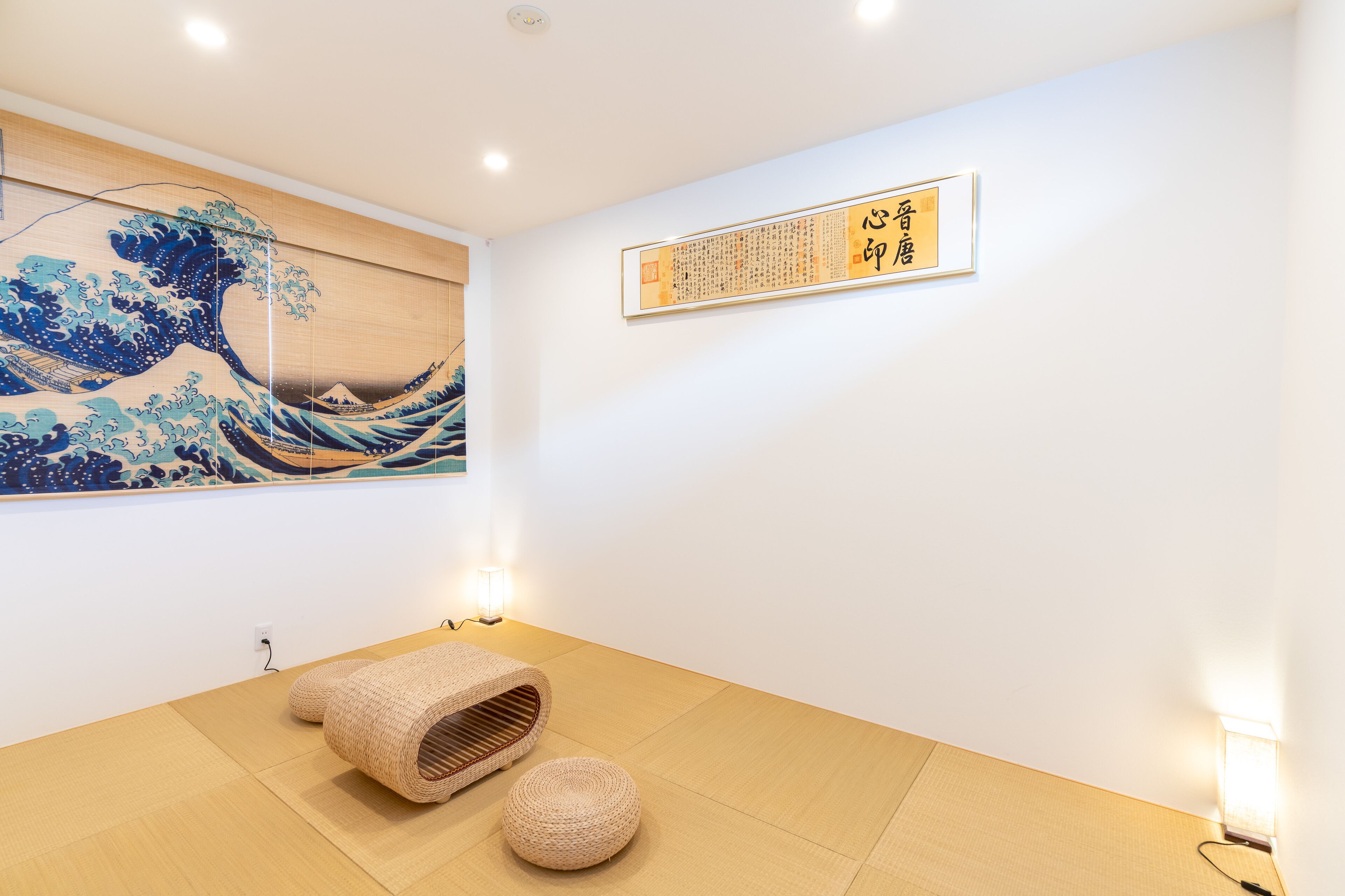 Una habitación con tatamis, un cuadro japonés con la imagen de una ola, una obra de caligrafía y una alfombra tejida en el suelo.
