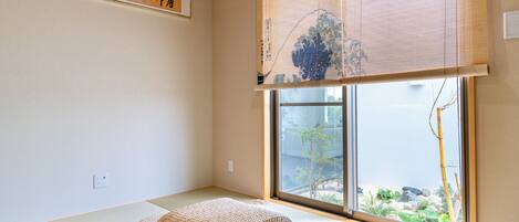 A traditional Japanese room with tatami flooring, a shoji screen, and a view of a garden through a sliding door.