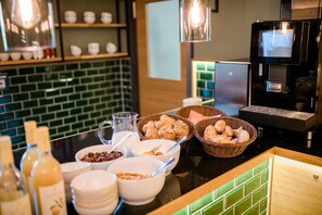 Un bufé de desayuno con distintos alimentos, una máquina de café y un respuesto de azulejos.
