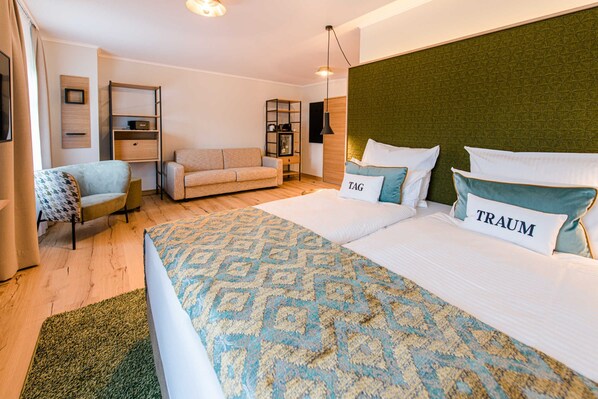 Una habitación de hotel moderna con una cama grande, un sofá, una mesita y una estantería.