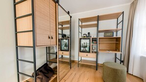 Una habitación con piso de madera, un reposapiés verde y dos estanterías de madera con puertas de vidrio que contienen botellas y un equipo de sonido.