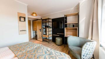 A compact bedroom with a bed, a chair, a wardrobe, and a desk area.