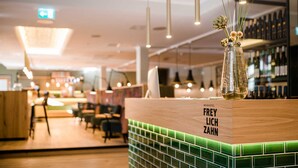 Una zona de bar con mostrador de azulejos verdes, luces colgantes y una exhibición de botellas de vino.