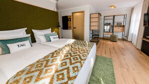 Habitación de hotel moderna con una cama grande, un cabecero verde, un escritorio con computadora y vista a la ciudad.