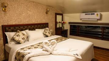 A neatly made bed with a heart-shaped towel, a wooden headboard, and a wall-mounted air conditioner.