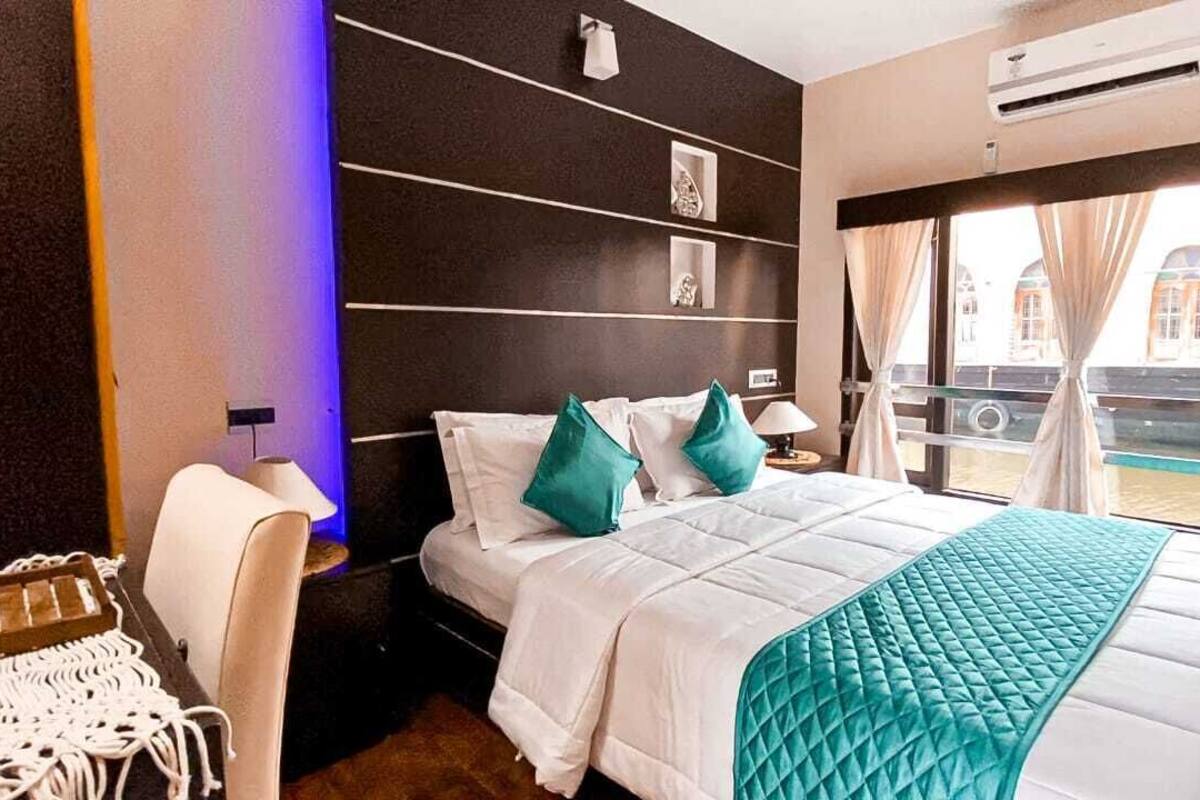 A hotel room with a bed, a chair, a nightstand, and a window with a view of buildings.