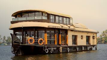 Una casa flotante con techo de paja, varias terrazas y una rueda hidráulica.