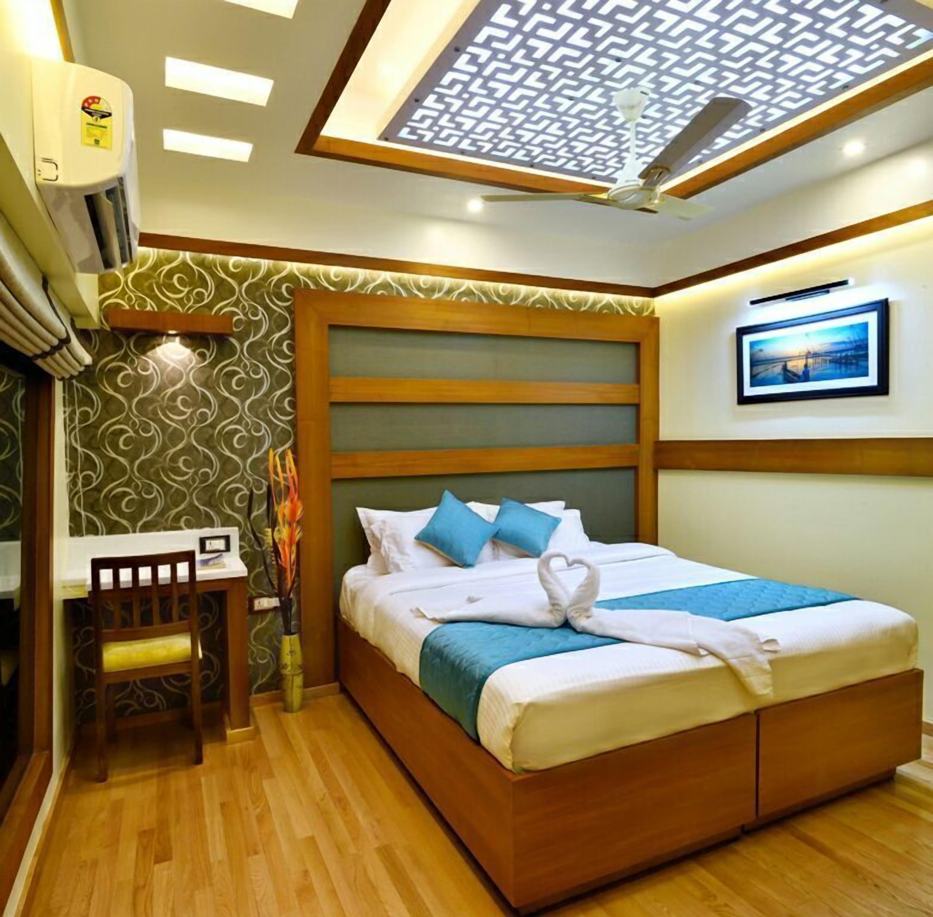 A hotel room with a bed, a desk, and a chair. There is a ceiling fan and an air conditioning unit.