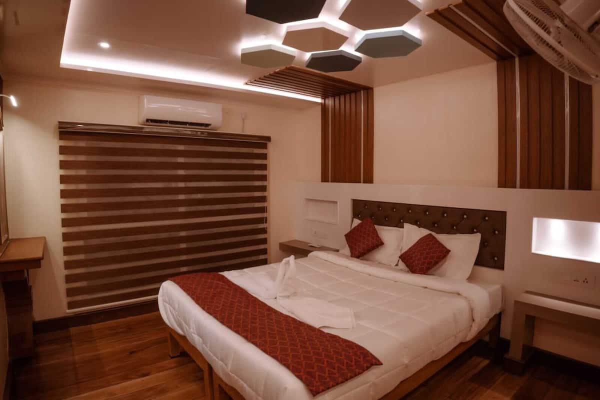 A modern bedroom with a large bed, wooden flooring, a slatted window blind, and a unique hexagonal ceiling design.