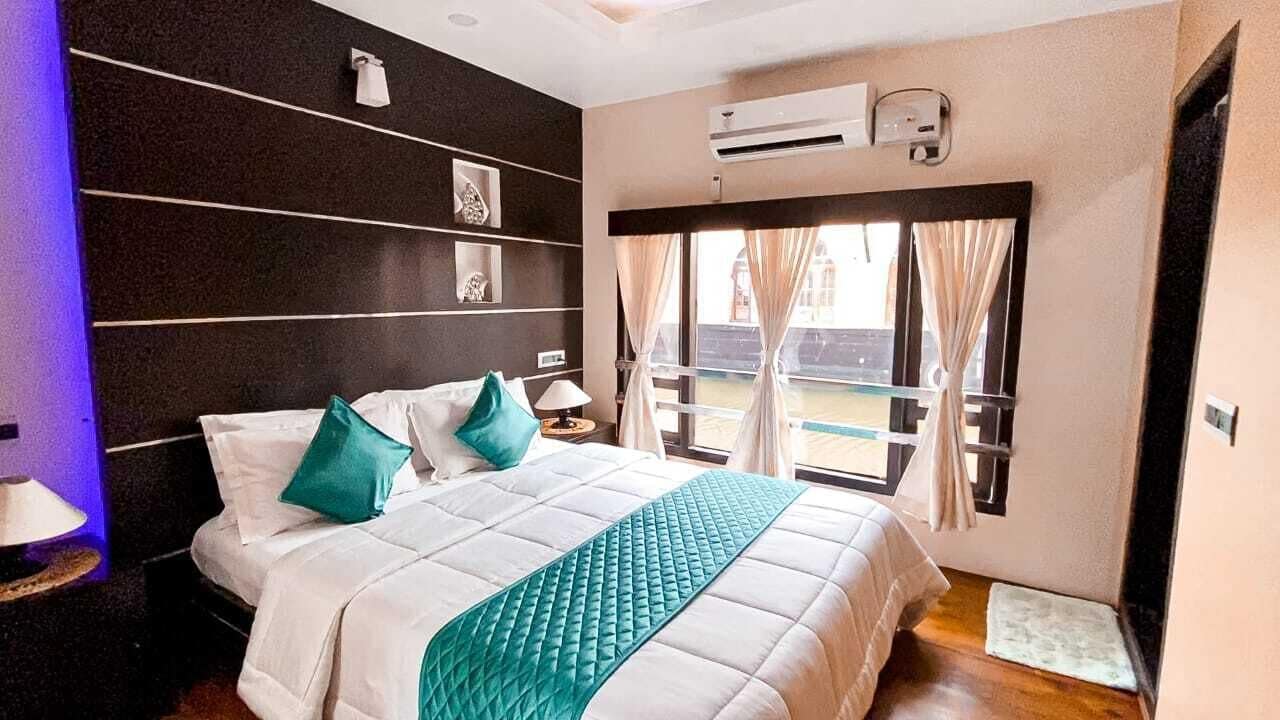 A hotel room with a bed, a nightstand, a window with curtains, and a wall-mounted air conditioning unit.