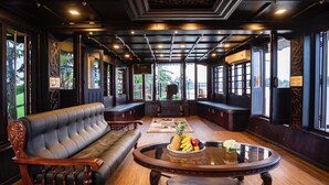 Una habitación amplia con un sofá de cuero, una mesa redonda de madera con fruta, y grandes ventanas que ofrecen vistas al exterior.