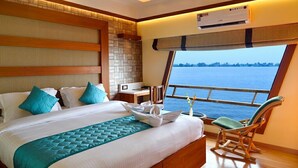 Habitación de hotel con una cama grande, cabecera de madera, ventana con vista al mar y ventilador de techo.