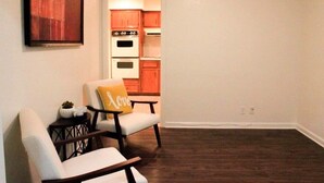 A living room with a sofa and armchair, a small table with a plant, and a kitchen visible through an open door. - The Minimalism near FC Q2✌🏻5 mins to Domain ATX ❤️ (Austin)