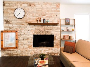 Un salon avec une cheminée en pierre, une horloge, une bibliothèque et un canapé.