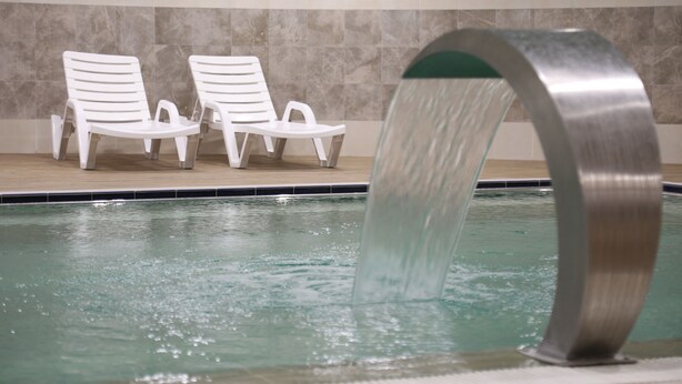 A swimming pool with a water feature and two white lounge chairs. - Ema Ozturk Thermal Hotel (Afyonkarahisar)