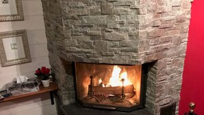 Une cheminée en pierre avec un feu qui crépite à l’intérieur, entourée d’un mur en pierre et d’un mur d’accent de couleur rouge.