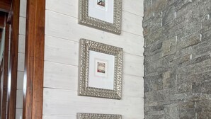 Un escalier avec une rampe en bois et un mur blanc orné de trois tableaux encadrés. Sous l’escalier, on trouve une étagère en bois sur laquelle sont posés une sculpture et un coussin moelleux de couleur grise.