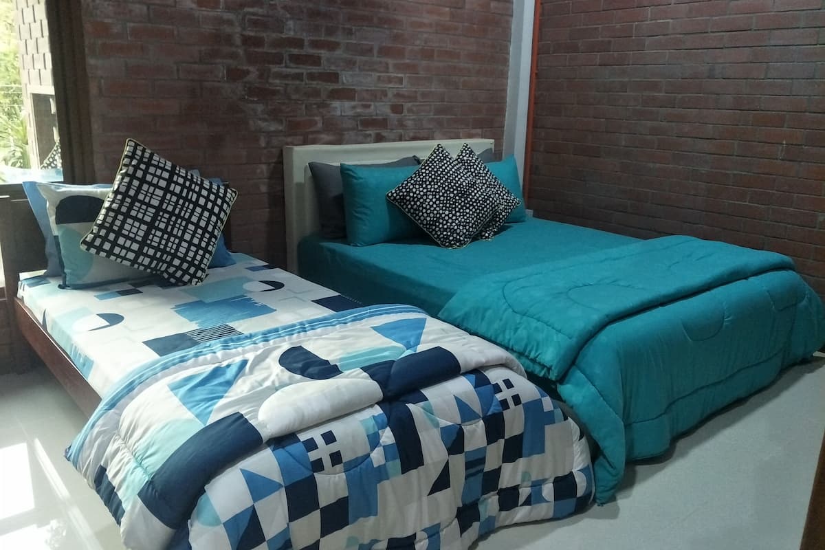 Una cama con colcha a cuadros azul y blanco y ropa de cama color verde azulado, cabecera de madera y pared de ladrillo.