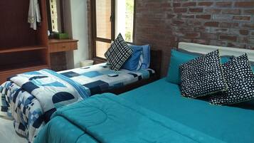 A bedroom with two beds, a brick wall, a window, and a wooden shelf.