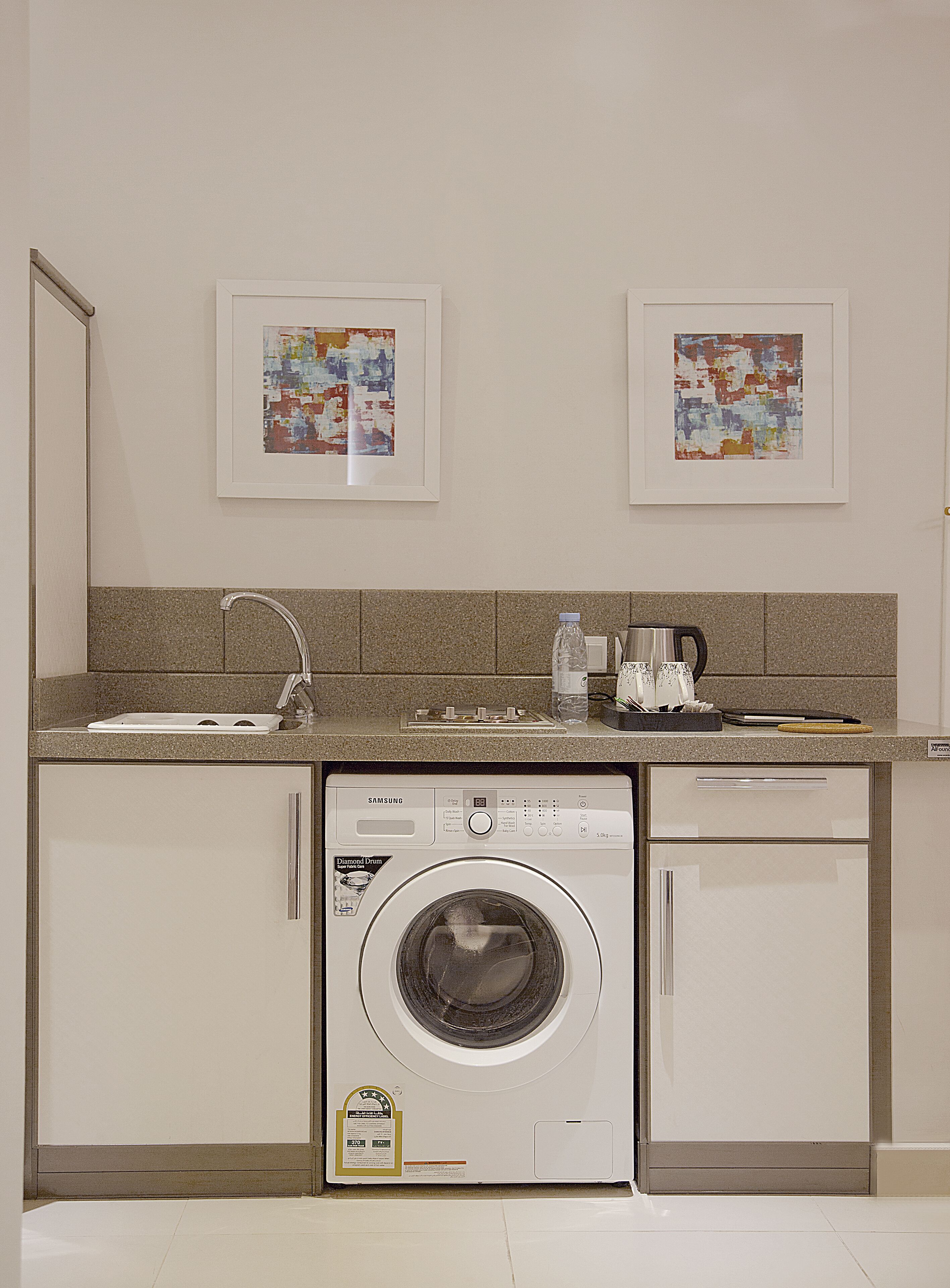 A compact kitchen with a built-in washer and dryer, a sink, and two framed artworks on the wall.