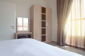 A bedroom with a bed, a wooden wardrobe, a desk, and a window with sheer curtains.