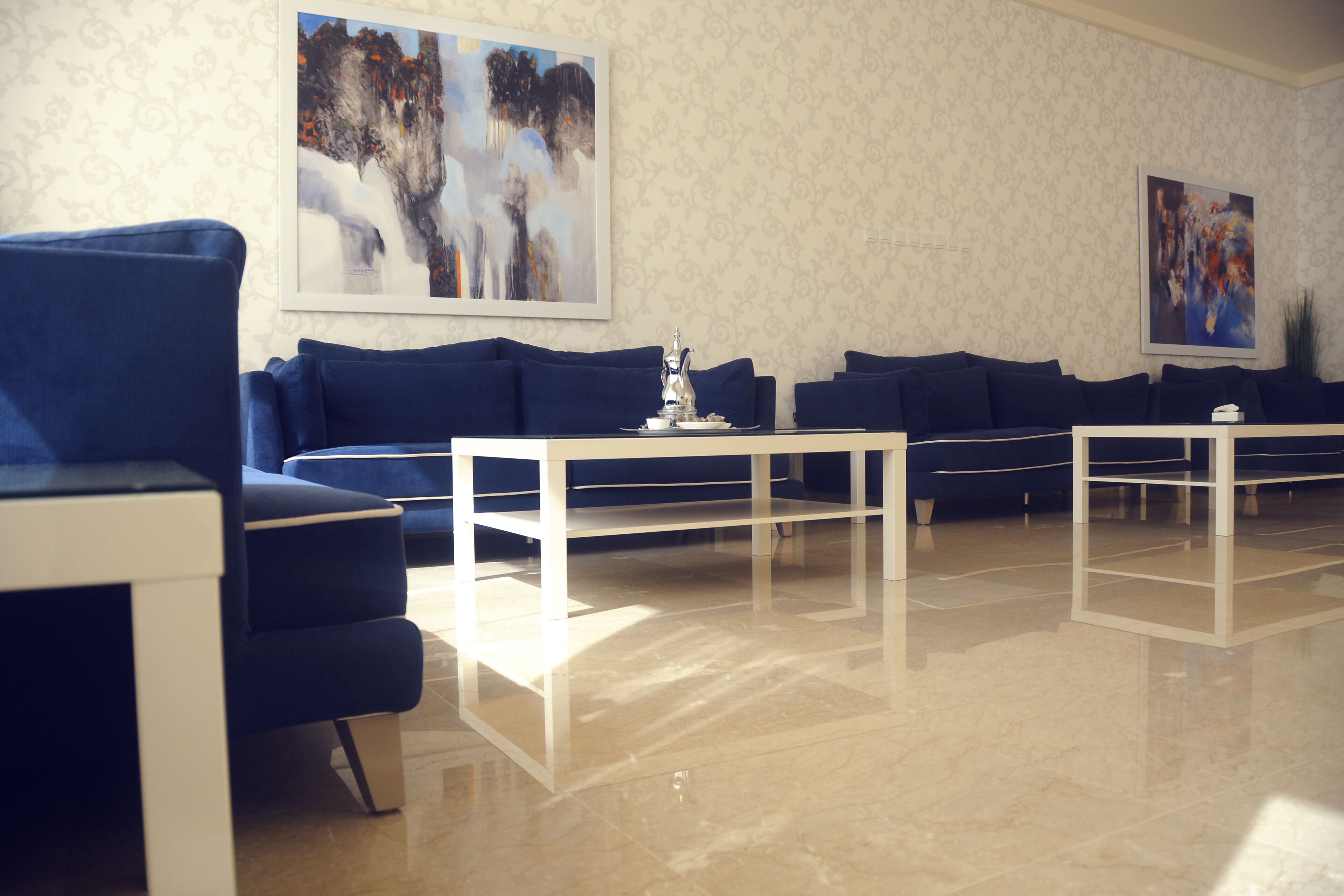 A modern lobby with blue sofas, white coffee tables, and abstract art on the walls.