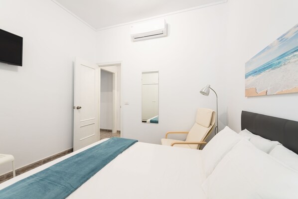 A hotel room with a bed, a chair, a desk, a TV, and a painting on the wall.
