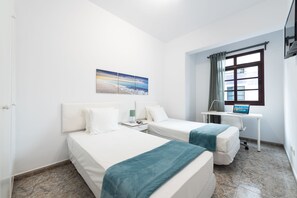 Een hotelkamer met twee bedden, een bureau, een computer en een raam met gordijnen.