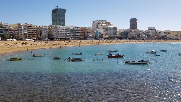 Un paysage urbain côtier avec une plage de sable, de nombreux bateaux et une variété de bâtiments, dont un grand gratte-ciel moderne.
