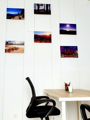 Een kamer met een witte muur versierd met zes ingelijste foto’s van verschillende landschappen, een tafel met een stoel, een potloodhouder en een klein decoratief object.