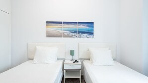 Une chambre d’hôtel avec deux lits, une table de chevet avec une lampe et un tableau représentant une scène de plage, accroché au mur.