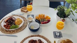 Une table mise pour le petit-déjeuner, avec une table ronde, des assiettes remplies de nourriture, un verre de jus d’orange et une plante en pot.