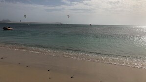 A beach with clear water, a boat, and people windsurfing. - Beautiful apartment 50 meters from the sea! (Sal Rei Boavista)