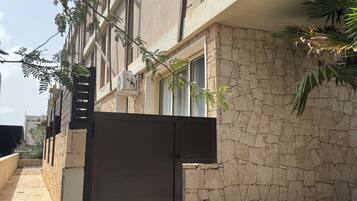 Un edificio de varios pisos con fachada de piedra, entrada protegida por una reja y un camino de acceso pavimentado.
