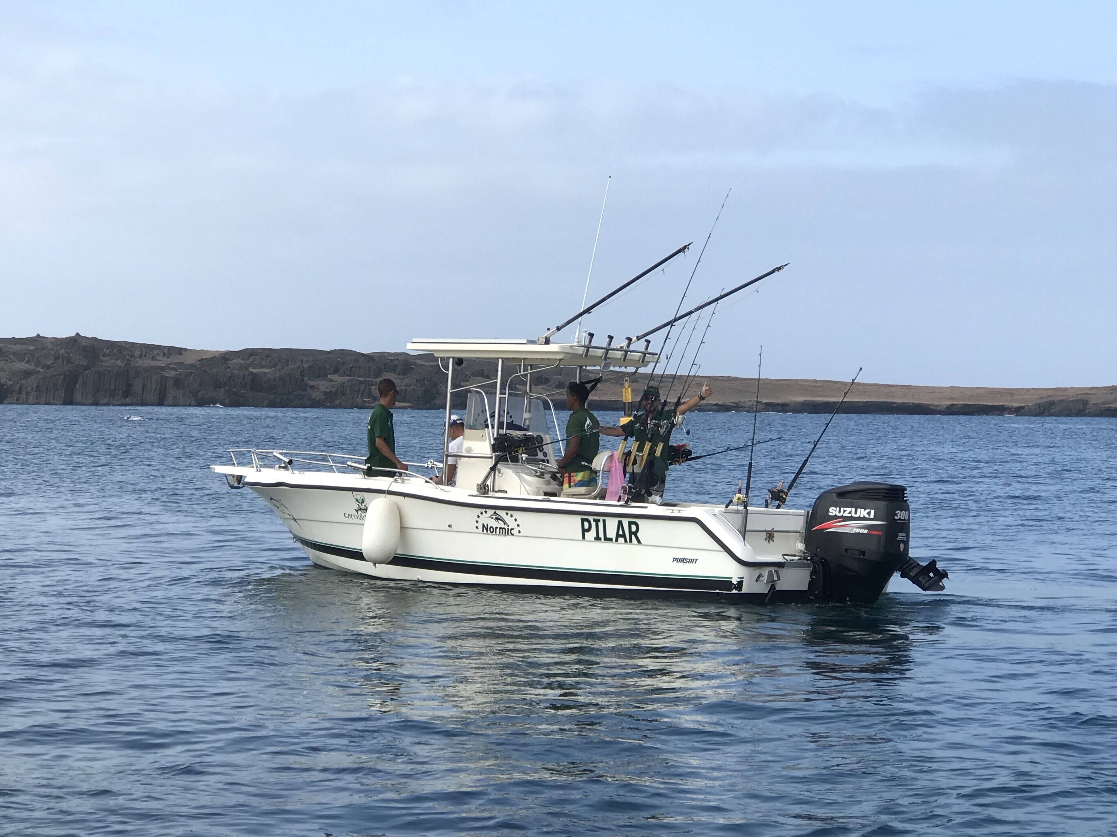 Un bote con el nombre 'PILAR' en su costado, equipado con cañas de pescar y un motor fueraborda Suzuki.