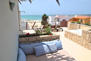 A balcony with a view of the beach, lounge chairs, and a stone wall. - Beautiful apartment 50 meters from the sea! (Sal Rei Boavista)