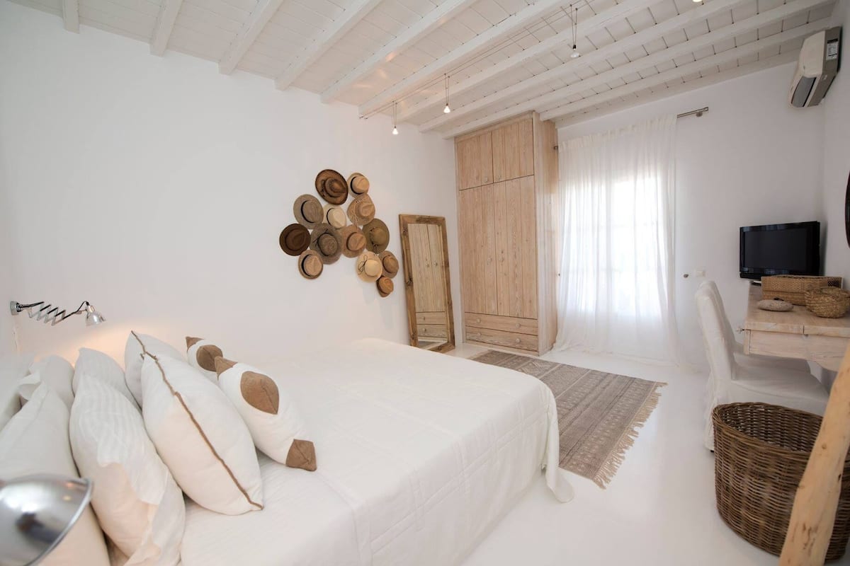 Un dormitorio con una cama grande, un armario de madera, un televisor y una cesta de mimbre.
