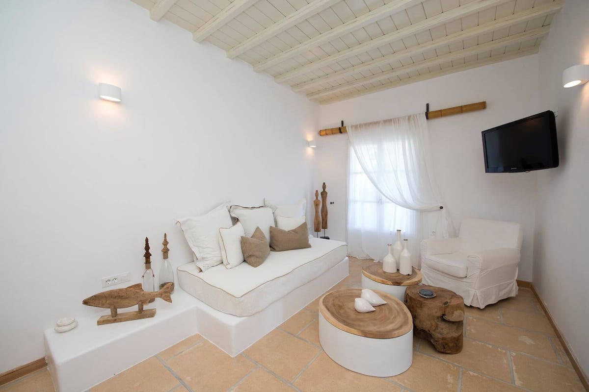Una habitación minimalista con un sofá blanco, un sillón blanco y un televisor fijado a la pared.
