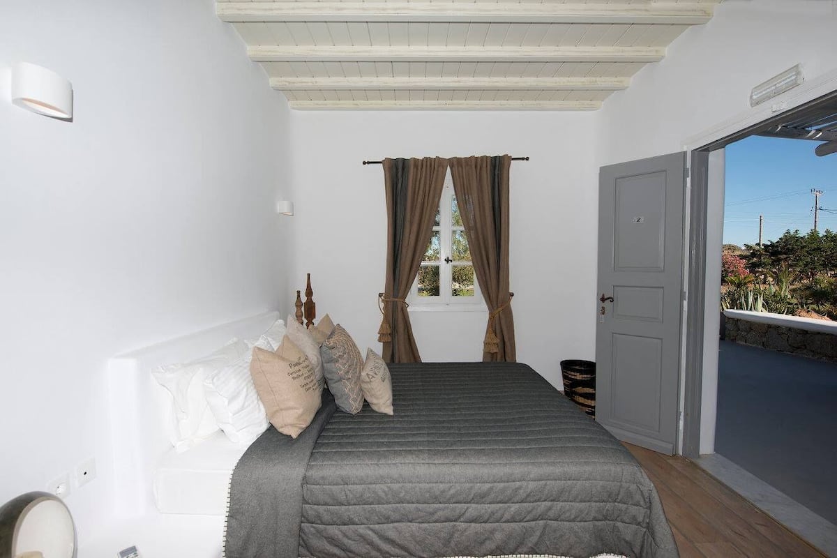 Un dormitorio con cama, ventana con cortinas, puerta y vistas al exterior.