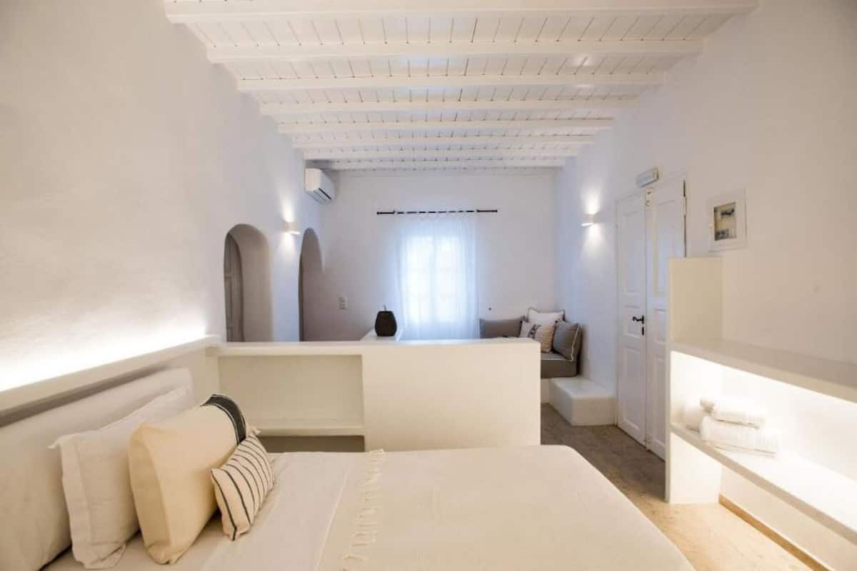 Un dormitorio con una cama grande, un escritorio y una silla. Hay una ventana con cortinas, una puerta y un aire acondicionado de pared.