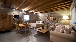 Una habitación acogedora con pared de piedra, vigas de madera en el techo, una mesa de madera con sillas, un sofá y un televisor fijado a la pared.