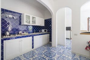 A kitchen with blue and white tiles, white cabinets, and a microwave. - Villa Carrino (Positano)