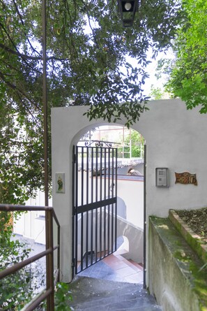 A gated entrance with a metal gate, a white wall, and a small sign. - Villa Carrino (Positano)