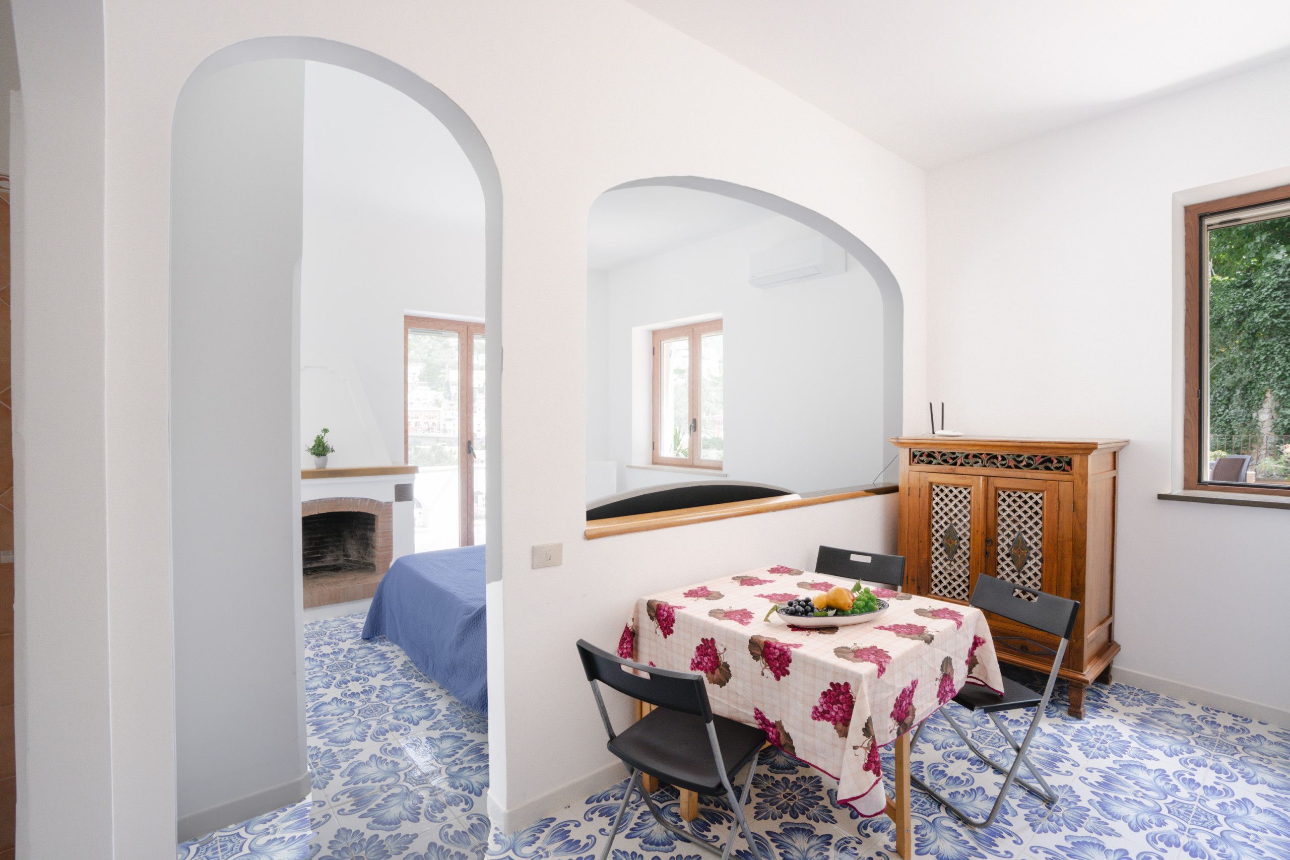 A dining area with a table set for two, a wooden cabinet, and a blue and white patterned floor.